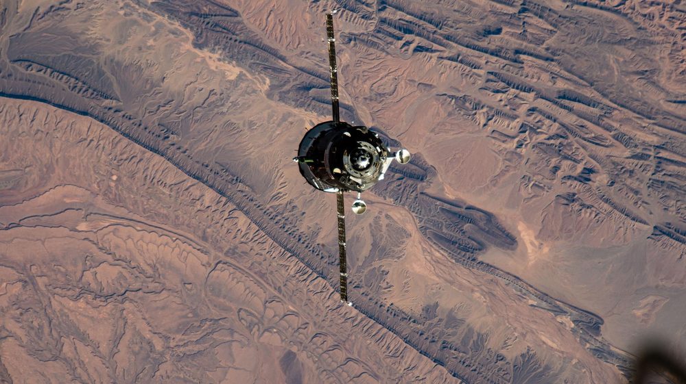 Spacecraft with two dark solar wings seen from above against ridged reddish desert