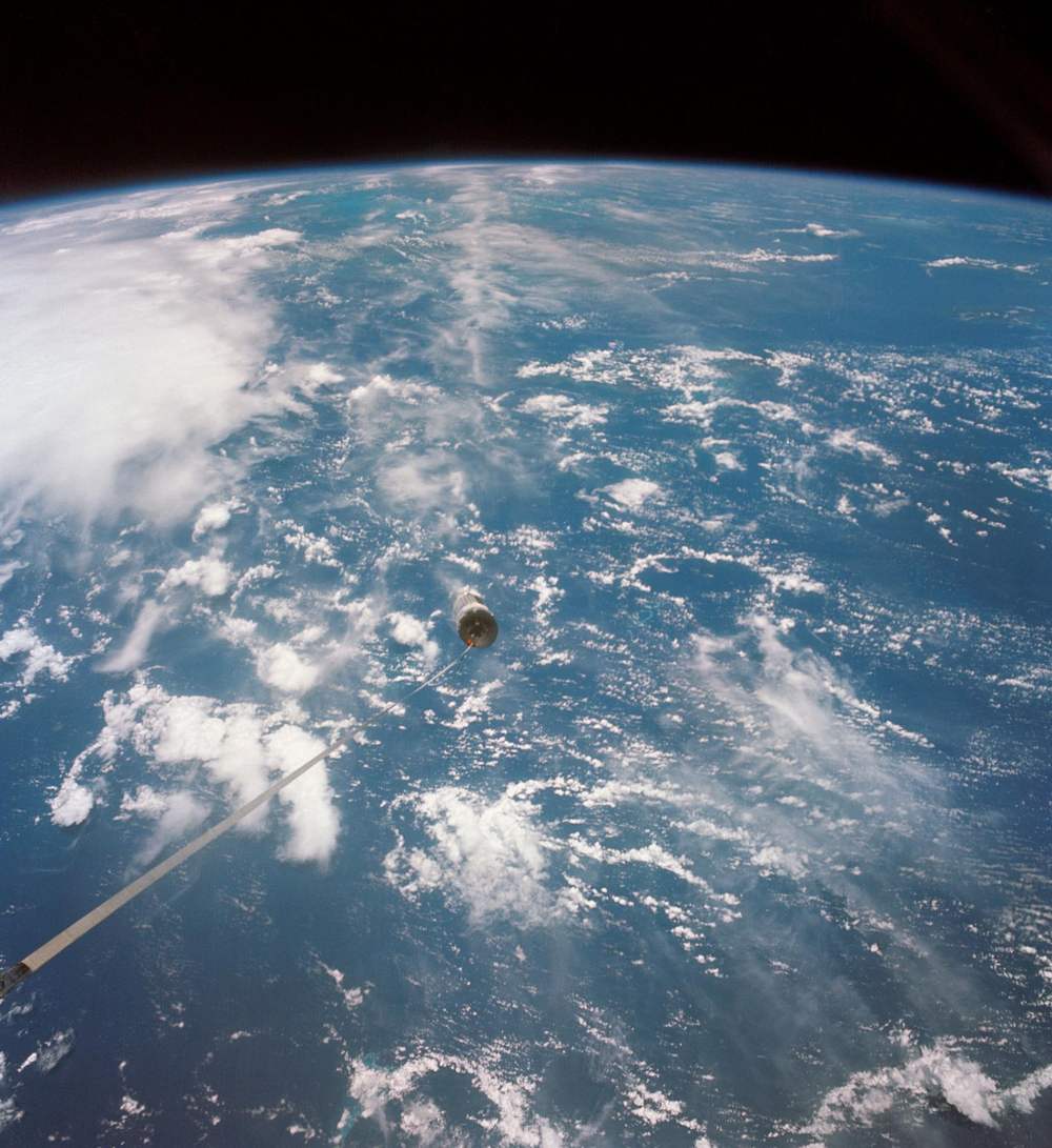 Cloud-flecked blue ocean fills the frame, a small distant vehicle above it, line trailing