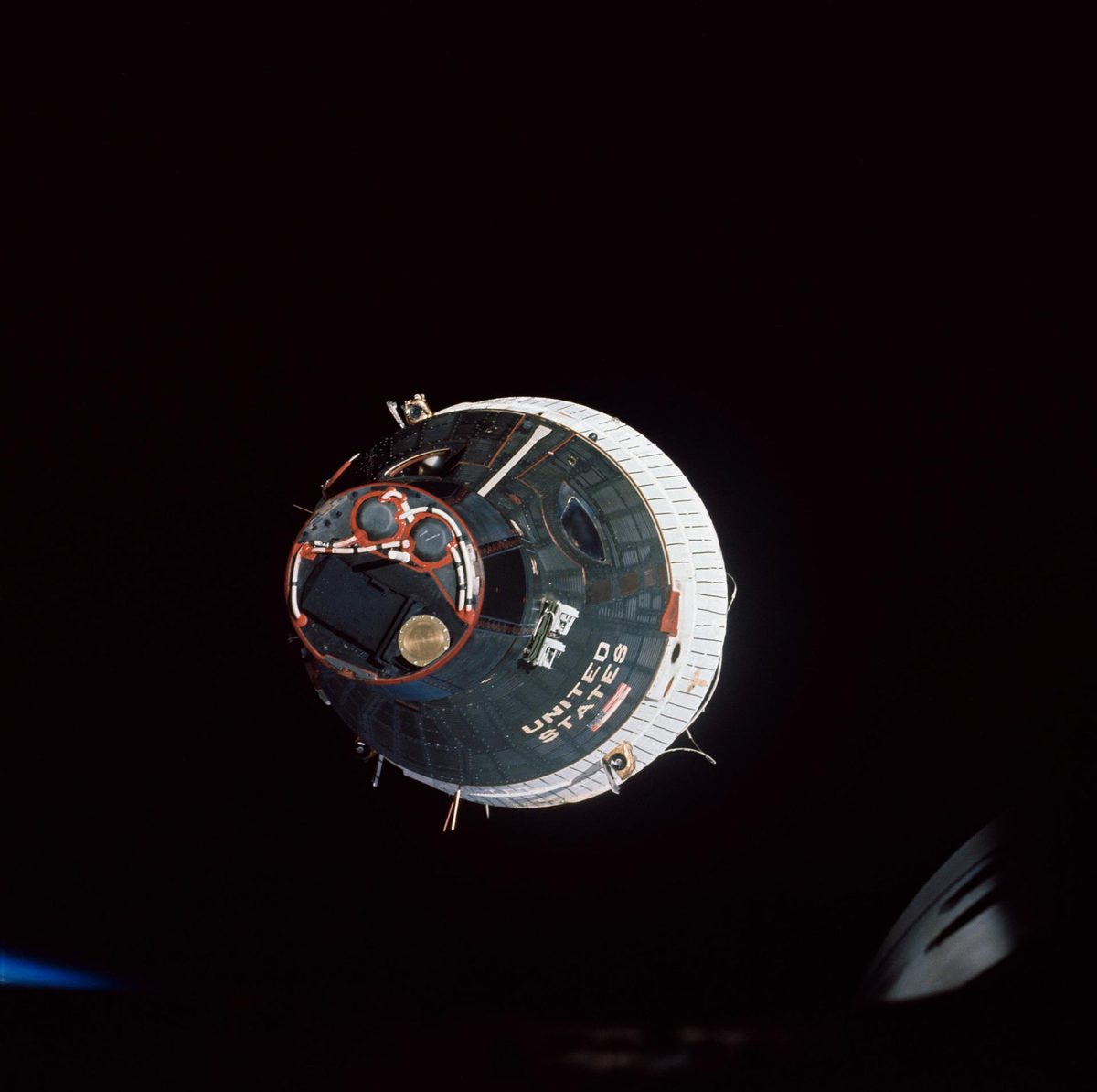 Two-seat capsule seen nose-on against black space, UNITED STATES lettering along its side