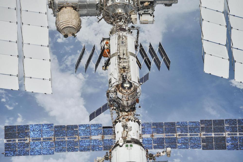 Stack of white modules with white radiators and blue solar arrays over bright cloud