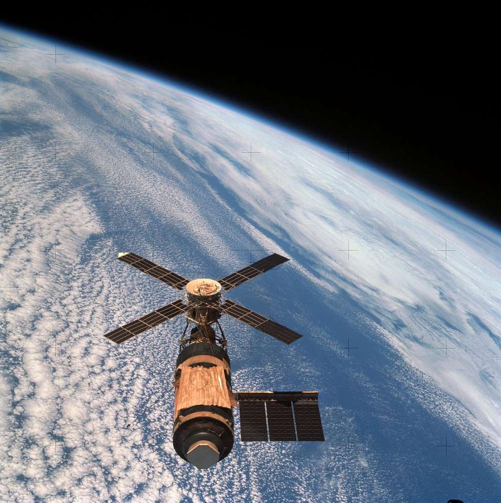 Station with a cross of four solar panels and a gold sunshade over cloud-flecked ocean