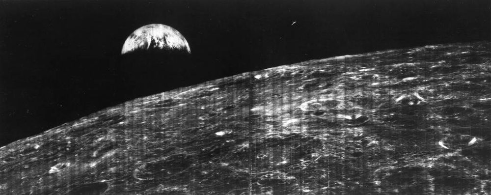 Half-lit Earth low over the lunar horizon in a wide monochrome strip, scan lines visible