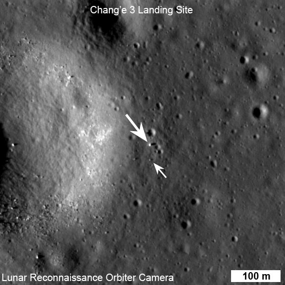 Grey orbital view of cratered ground, two white arrows pointing at tiny bright specks