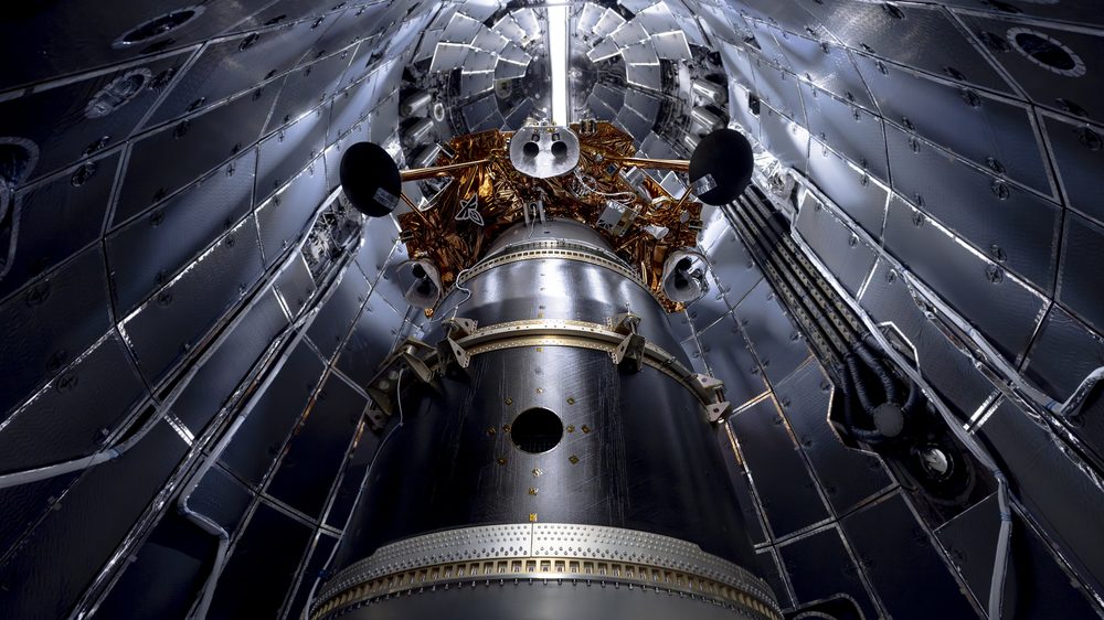 Looking up inside a silver fairing at a gold-wrapped payload on a cylindrical adapter