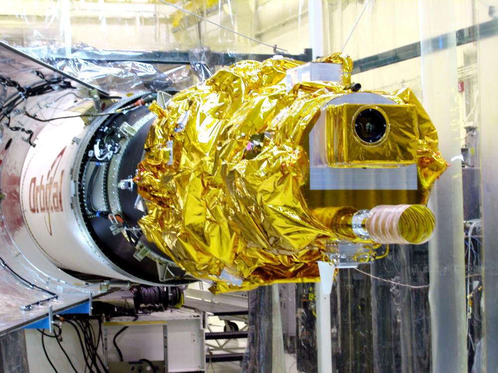 Gold foil-wrapped spacecraft mated to a white upper stage inside a hangar, lens aperture visible