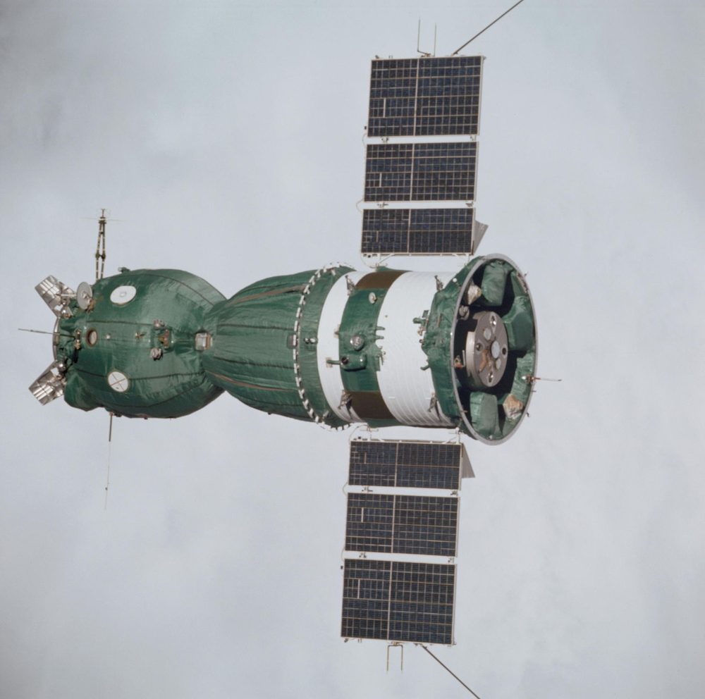 Green quilted spacecraft with two solar wings, its docking mechanism turned towards the camera