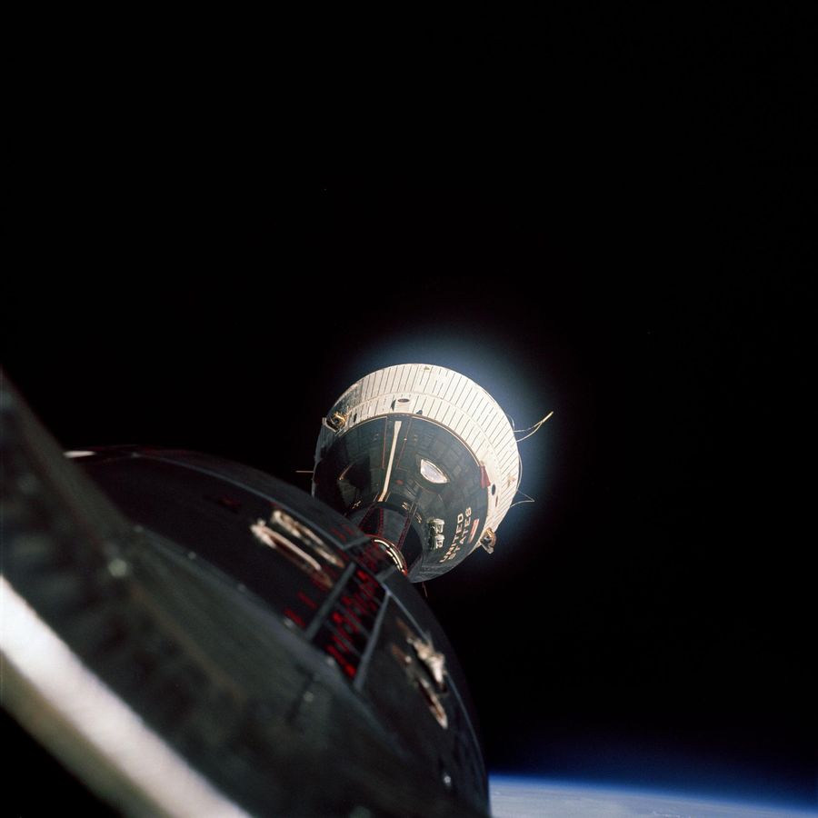 Distant capsule with a white shingled adapter section, the photographing spacecraft’s nose in the foreground