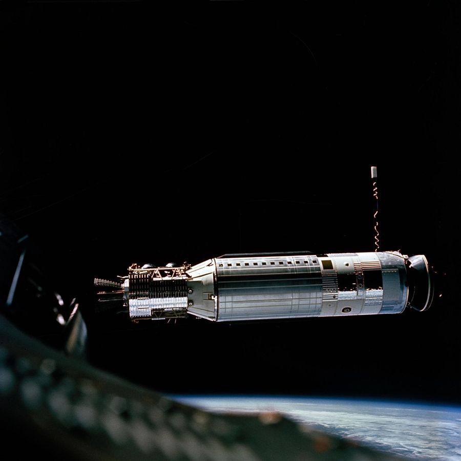 Slender silver cylinder side-on with a docking cone at one end, blue Earth below
