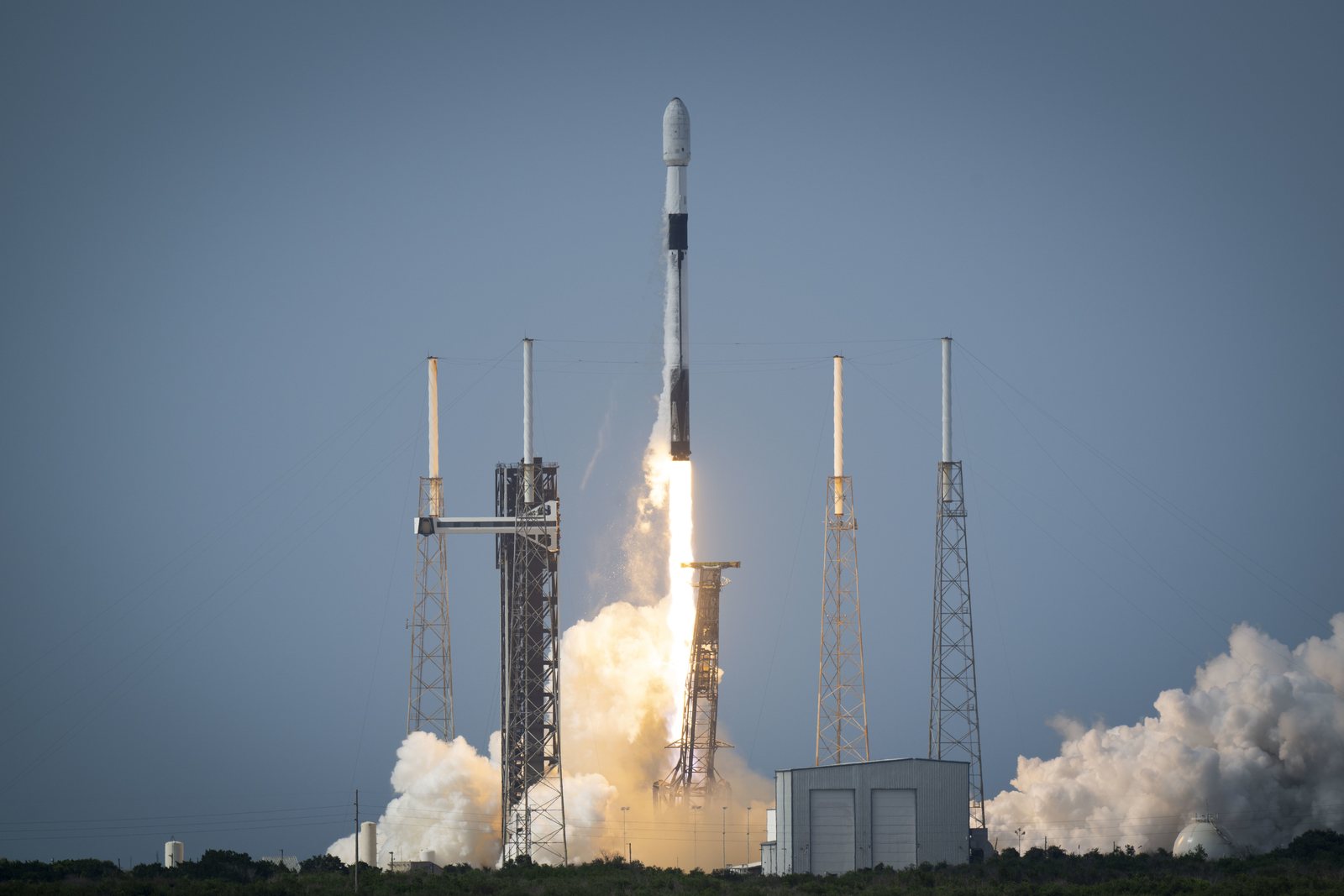 Falcon 9 climbing on a long bright exhaust plume against a pale sky