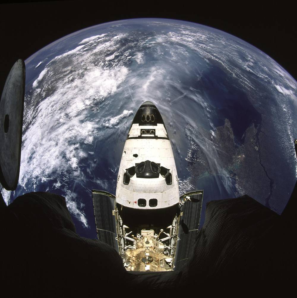 Fisheye view down onto an orbiter’s nose and open payload bay, Earth curving behind