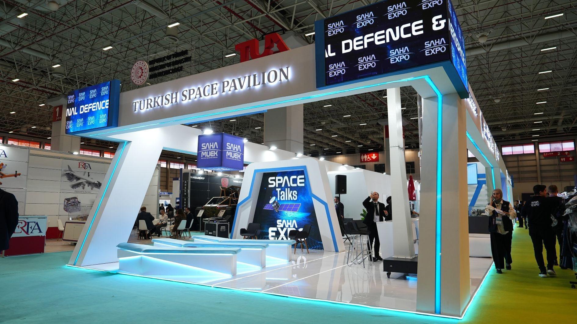 The Turkish Space Pavilion stand, a white structure edged in cyan light under a TUA sign, a Space Talks screen inside